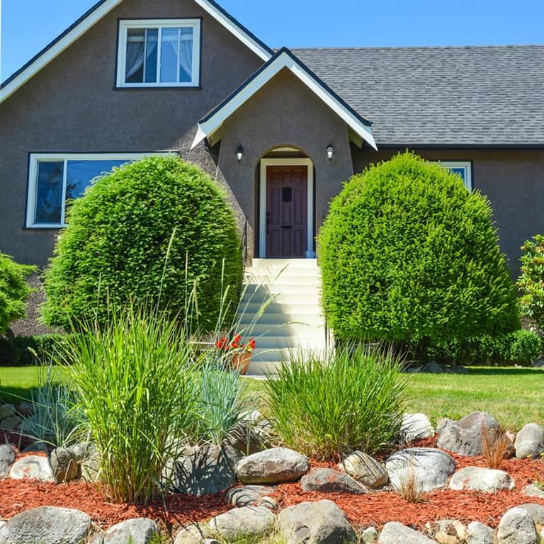 Front yard of a home with green lawn, neatly trimmed shrubs, and a curved garden bed.
